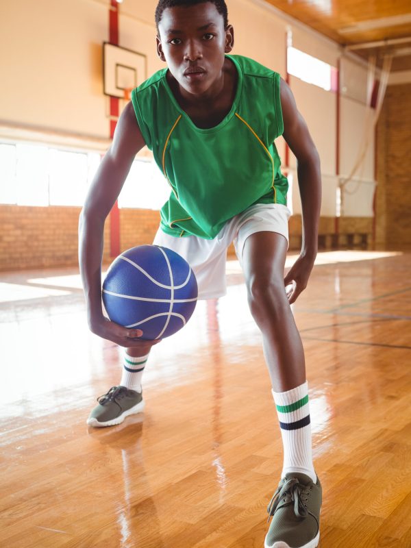Portrait of teenage boy playing basketball in court